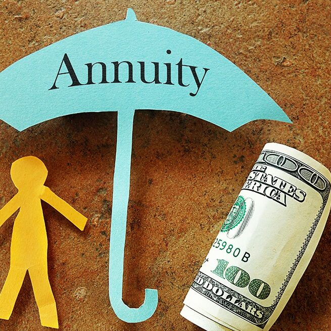 paper cut out stick figure and a rolled up hundred dollar bill sheltered under a paper cut umbrella labeled annuity